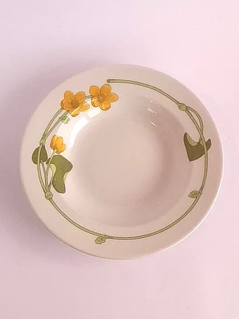 White soup plate with Art Nouveau-style marsh marigold decoration featuring yellow flowers and curving green stems