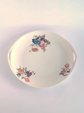 Round white porcelain serving platter with two handles, decorated with colorful floral bouquets in pink, blue, and orange