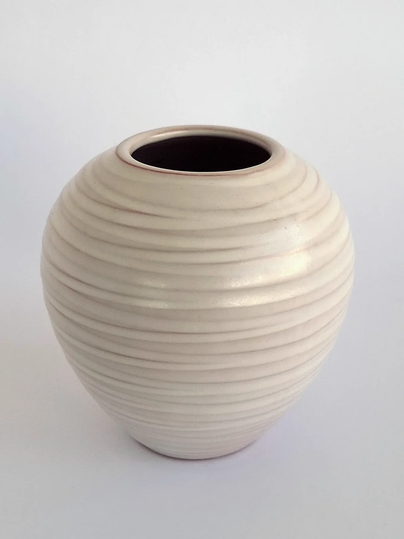 Rounded earthenware vase with horizontal ribbed texture and off-white glaze, showing warm terracotta clay at the edges where the glaze is thin